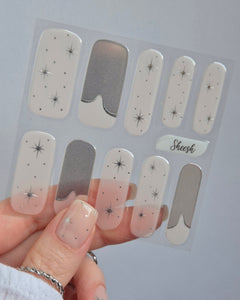 Sheesh Nails – Cosmic Crush – transparente Nagelfolien mit silbernem Glitzer und funkelnden Sternmotiven, elegantes Design für festliche Maniküren. Perfekte Passform und glänzendes Finish für einen modernen, glamourösen Nailart-Look.