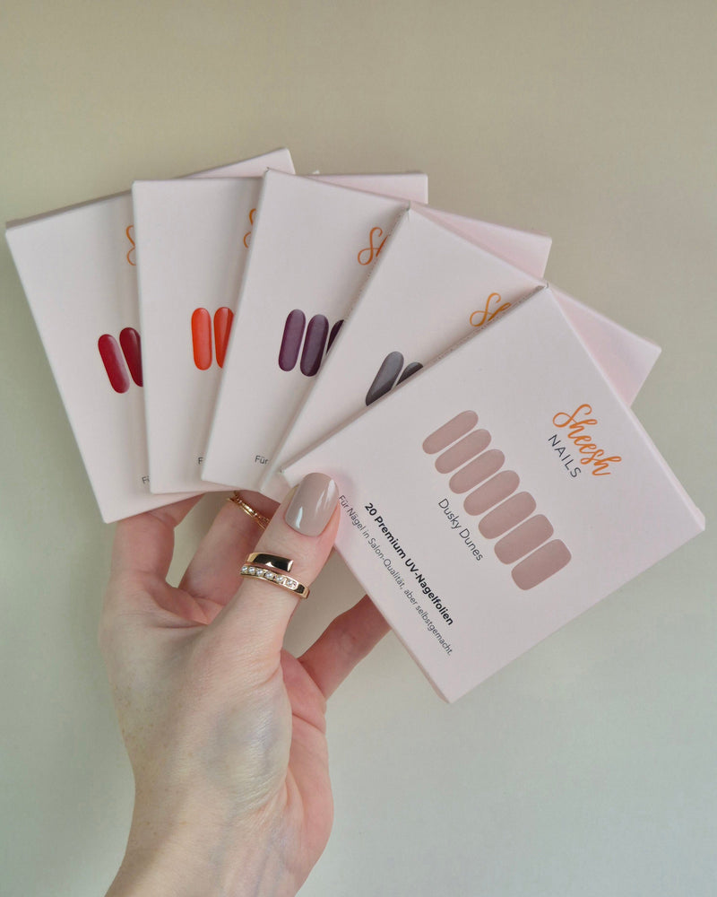 Sheesh UV-Nagelfolien 5er Set – Hand hält fünf verschiedene Sheesh Nagelfolien-Verpackungen in Salonqualität für individuelle Maniküre.