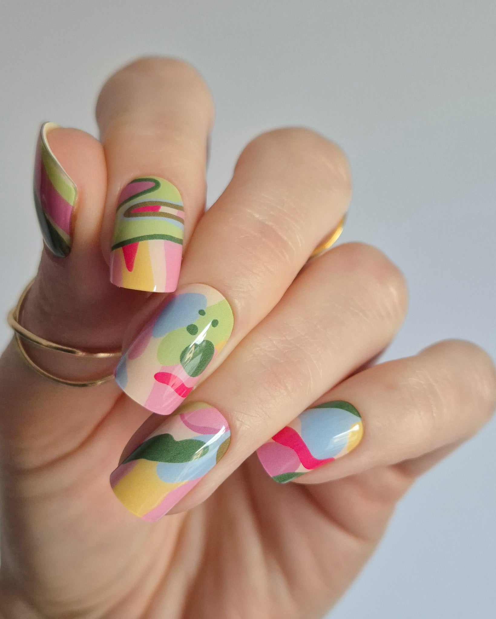 Arty UV-Nagelfolie mit buntem abstraktem Design auf Hand vor hellem Hintergrund