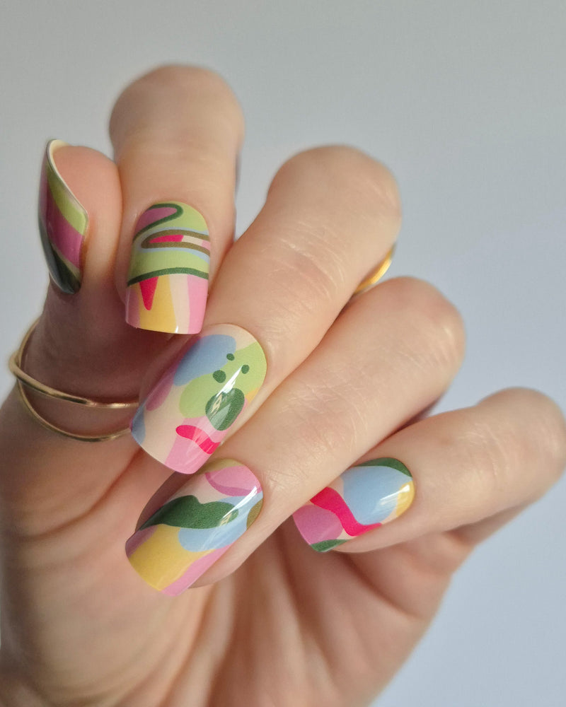 Arty UV-Nagelfolie mit buntem abstraktem Design auf Hand vor hellem Hintergrund