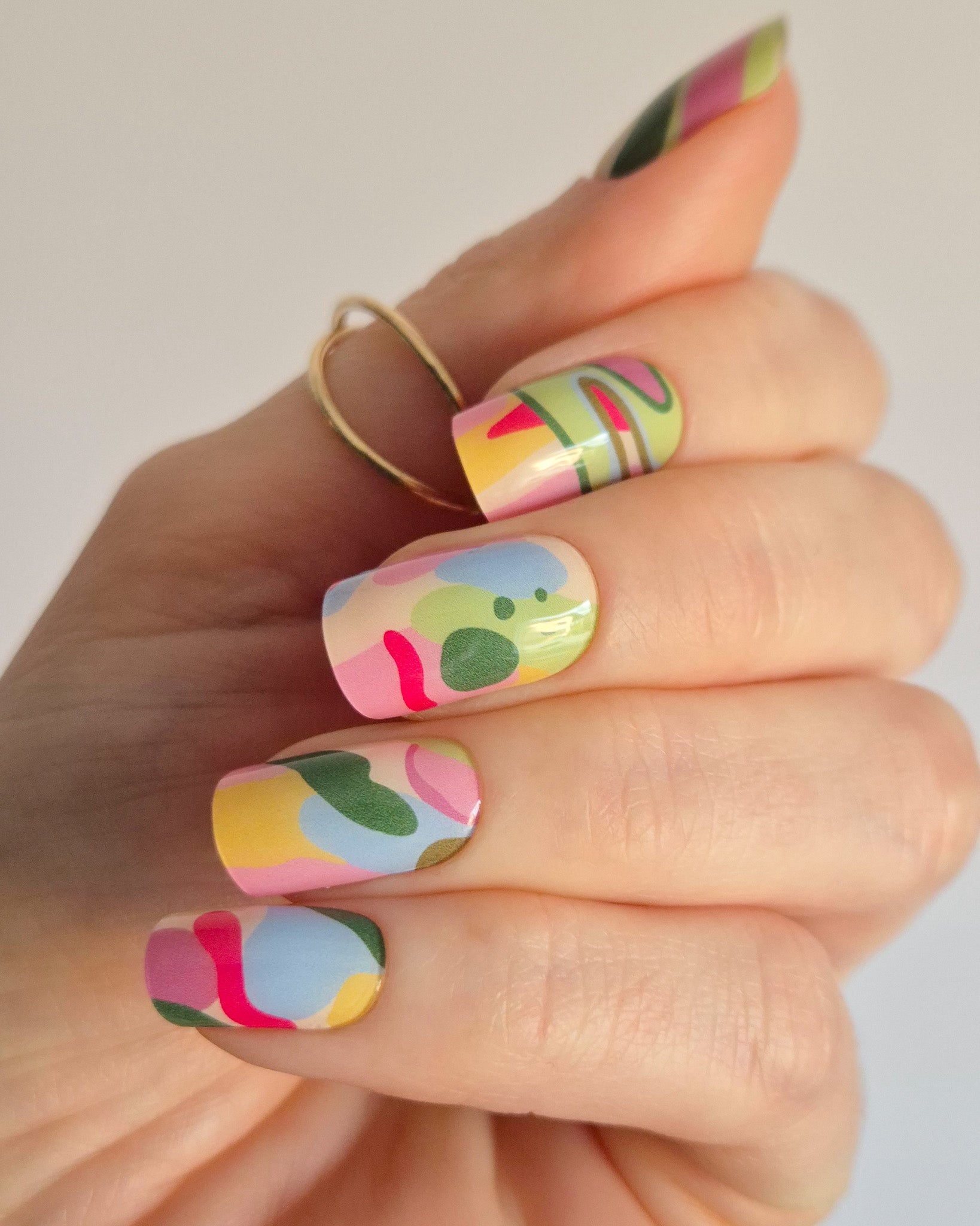 Arty UV-Nagelfolie mit buntem abstraktem Design auf Hand vor hellem Hintergrund