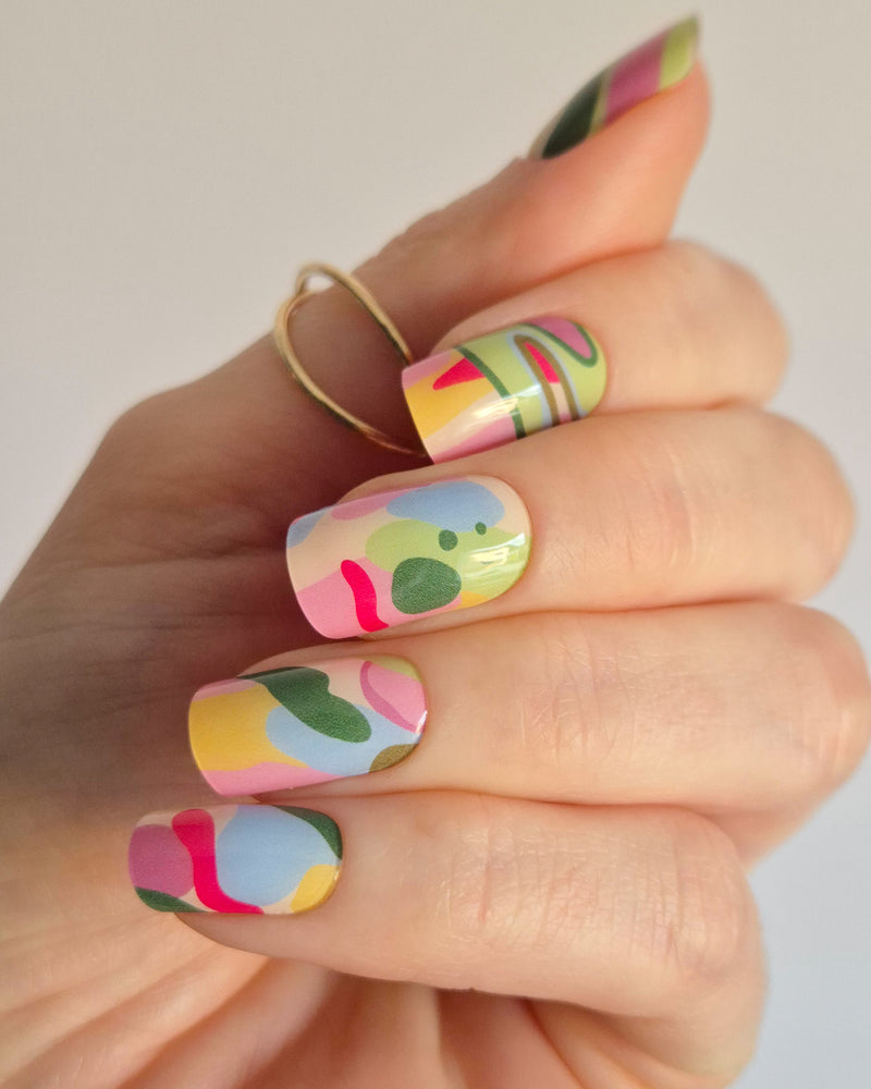Arty UV-Nagelfolie mit buntem abstraktem Design auf Hand vor hellem Hintergrund