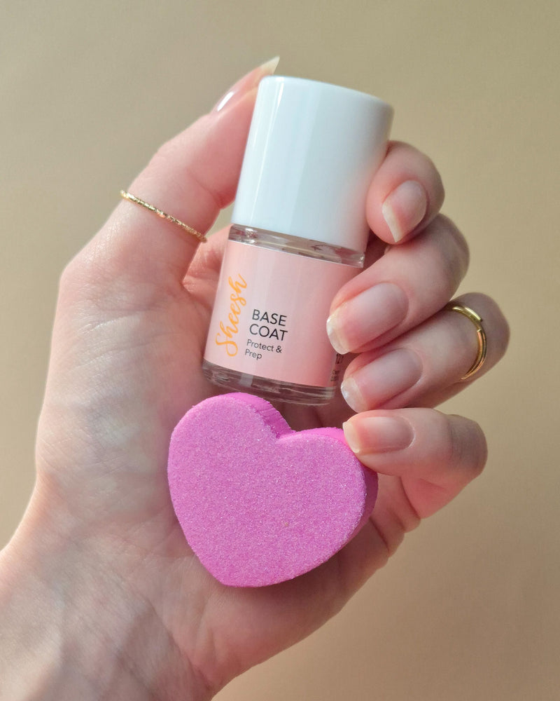 SHEESH Nails Base Coat wird mit Pinsel auf einen Fingernagel aufgetragen vor hellem Studiohintergrund