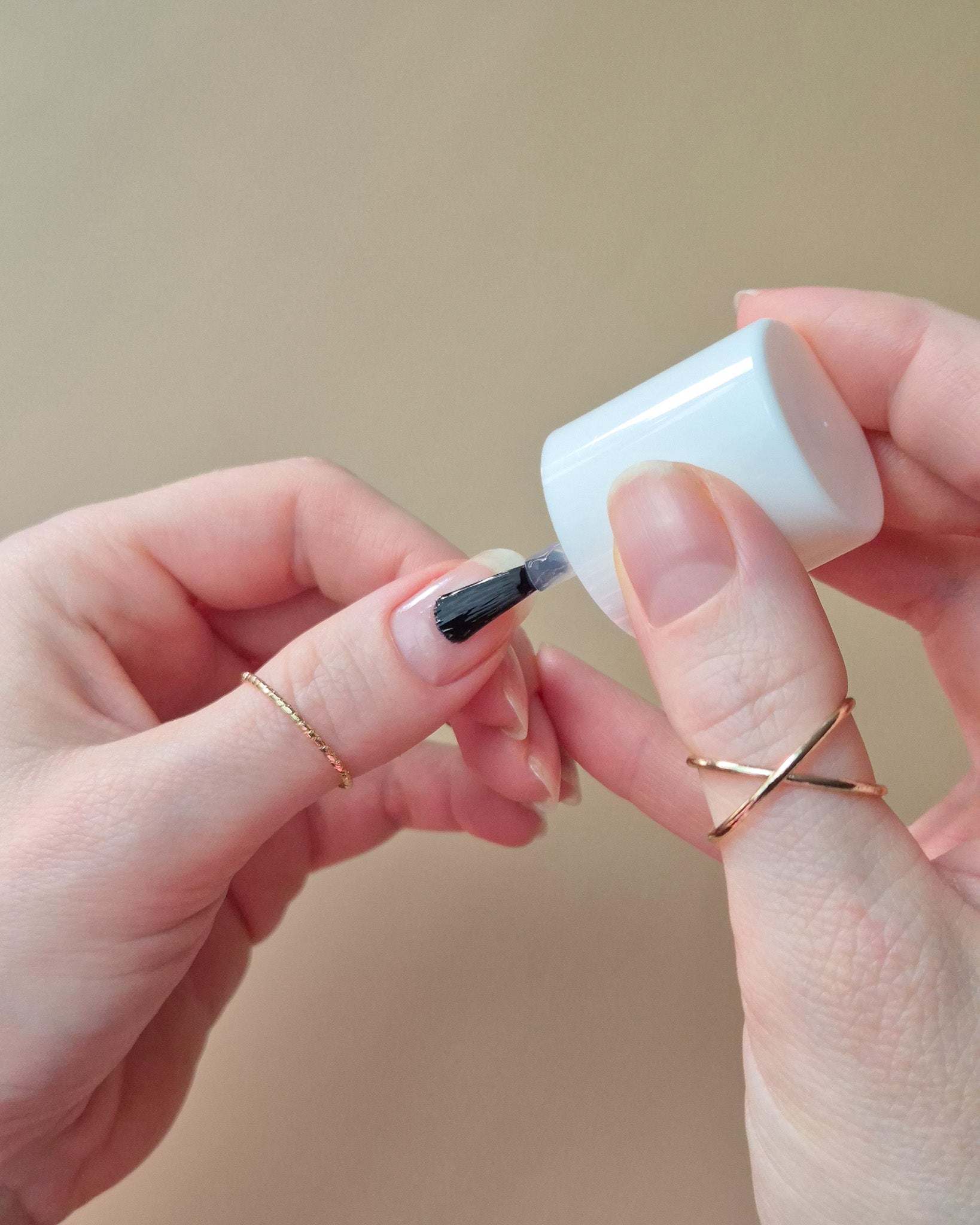 SHEESH Nails Base Coat wird mit Pinsel auf einen Fingernagel aufgetragen vor hellem Studiohintergrund