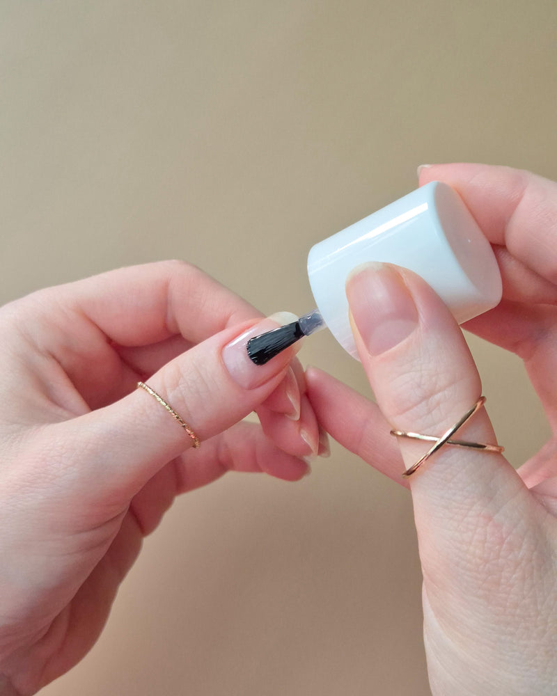SHEESH Nails Base Coat wird mit Pinsel auf einen Fingernagel aufgetragen vor hellem Studiohintergrund
