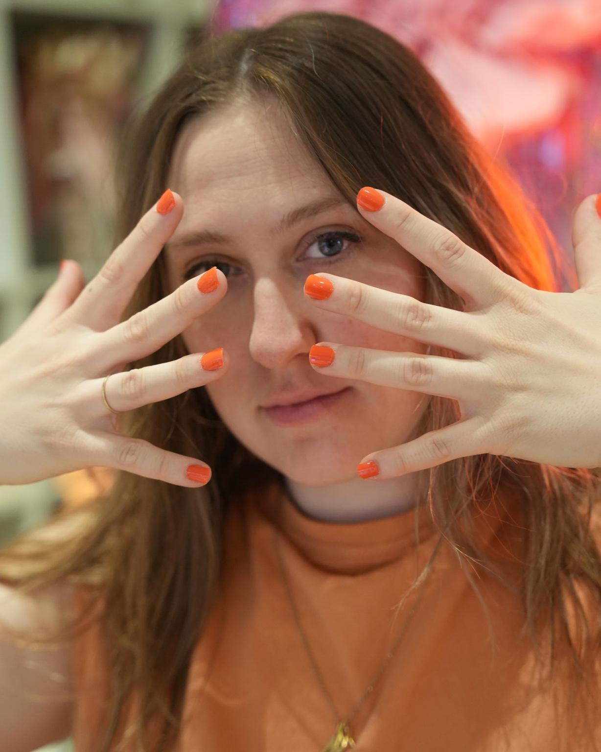 Sheesh Nails – Kundin trägt Blood Orange Mimosa UV-Nagelfolien in leuchtendem Korallton. Zeigt das natürliche Trageergebnis der glänzenden, UV-härtenden Sheesh Nails Folien mit gepflegtem, modernen Look – ideal für sommerliche Maniküren mit frischer Ausstrahlung.