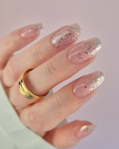 Nahaufnahme einer Hand mit der Sheesh Nails UV-Nagelfolie „Champagne Fizz“. Die Nägel zeigen ein zartes Nude-Rosa, das sanft in funkelnden Silberglitter übergeht. Der Look wirkt edel, festlich und feminin – perfekt für elegante Anlässe, festliche Looks oder einen stilvollen Alltagsglanz.