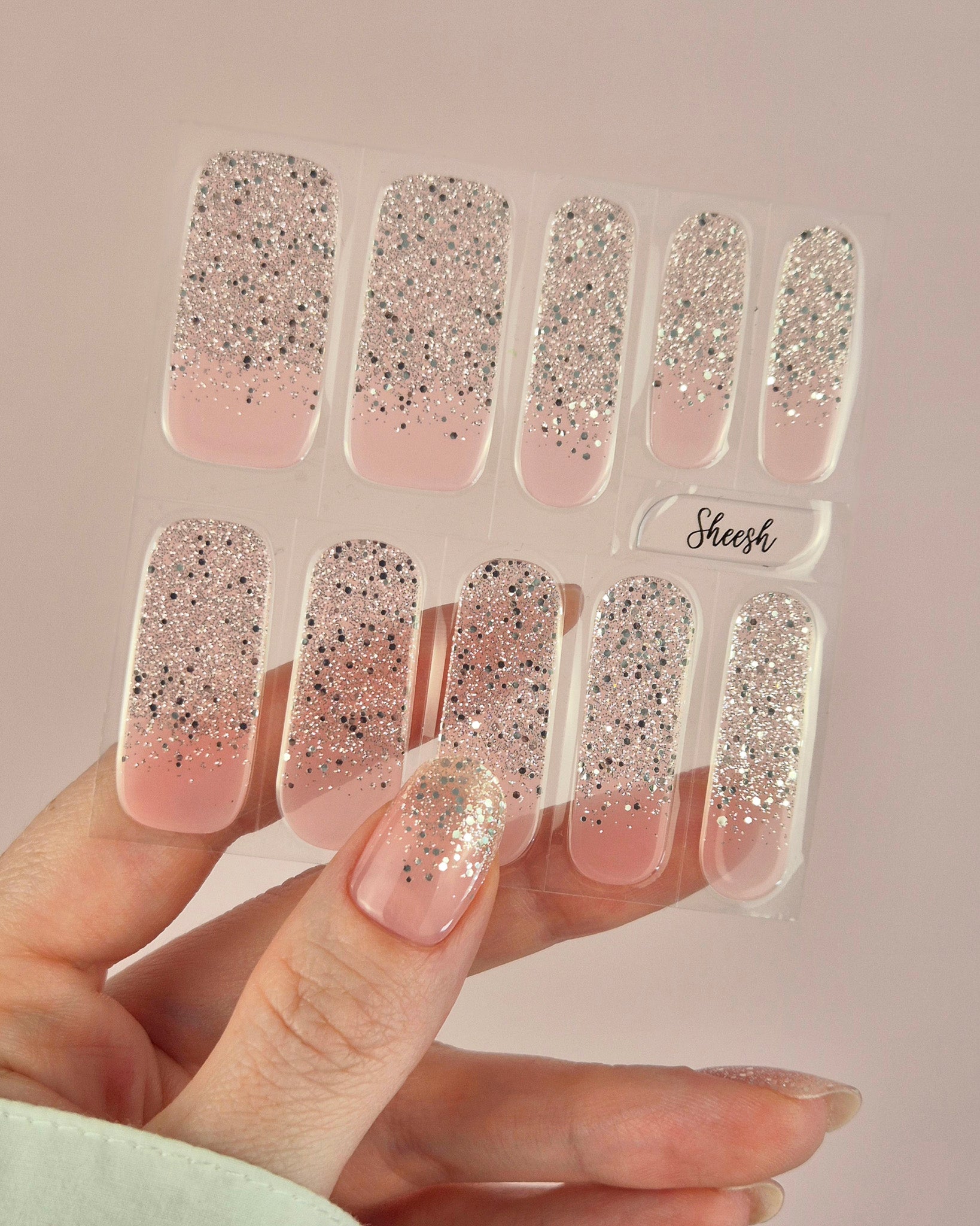 Nahaufnahme einer Hand mit der Sheesh Nails UV-Nagelfolie „Champagne Fizz“. Die Nägel zeigen ein zartes Nude-Rosa, das sanft in funkelnden Silberglitter übergeht. Der Look wirkt edel, festlich und feminin – perfekt für elegante Anlässe, festliche Looks oder einen stilvollen Alltagsglanz.