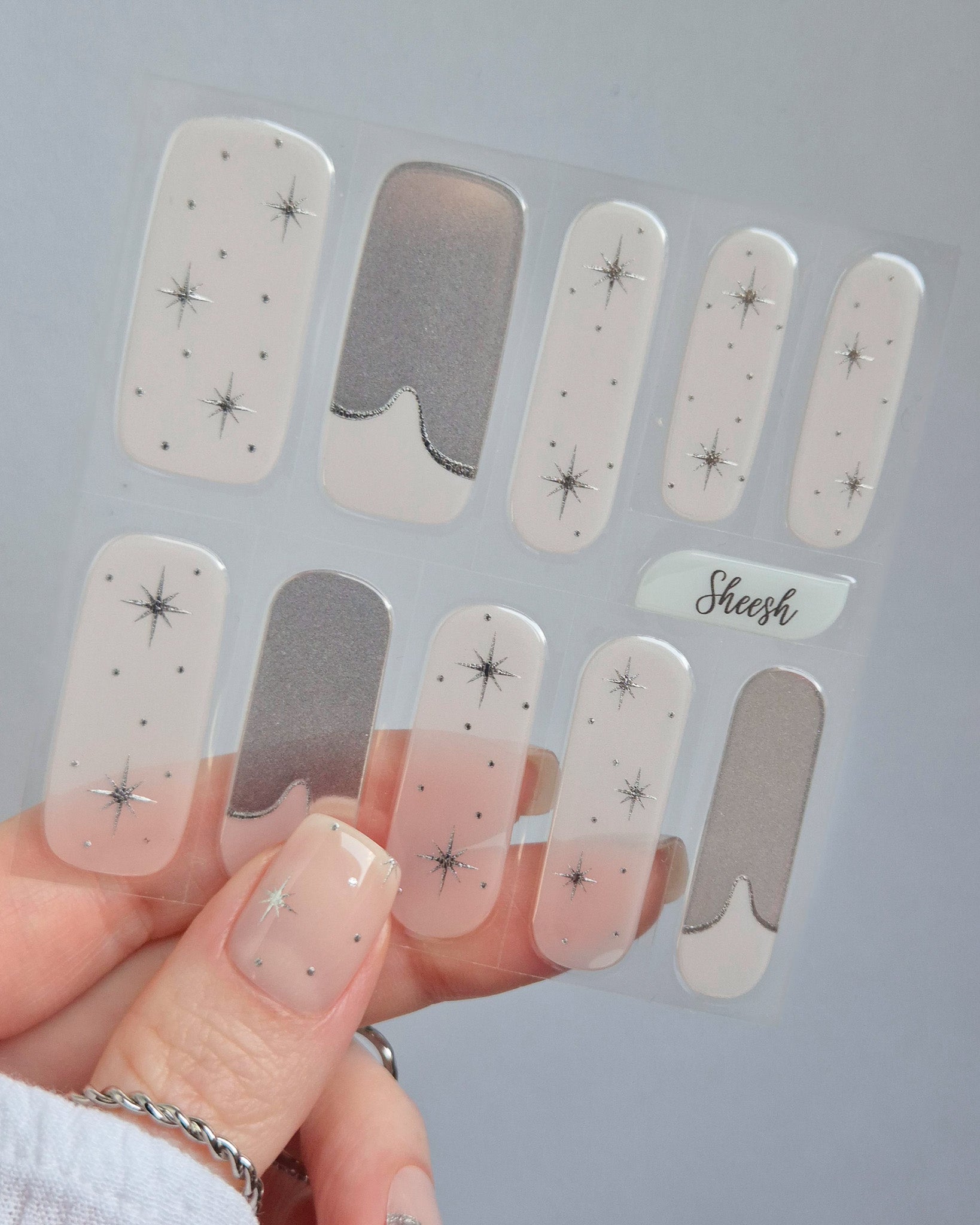 Sheesh Nails – Cosmic Crush – elegante Nagelfolien in transparentem Nude mit silbernem Glitzer und funkelnden Sternmotiven, stilvolles Design für moderne, glamouröse Maniküren. Perfekte Passform und glänzendes Finish für festliche Looks.