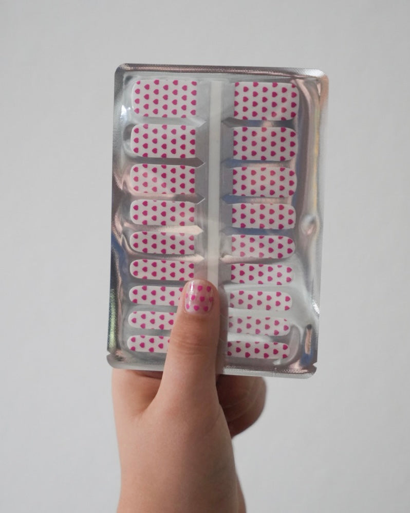 Kinderhand hält ein Set der Sheesh Nails Kinderfolie „Love“. Die Nagelfolien zeigen rosa Herzen auf transparentem Untergrund und funkeln dezent im Licht. Das verspielte Design vermittelt Liebe, Freude und Kreativität – ideal für Kinder, die zarte Farben und niedliche Motive lieben.