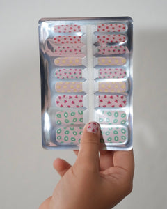 Kinderhand hält ein Set der Sheesh Nails Kinderfolie „Süße Früchtchen“. Die bunten Nagelfolien zeigen kleine Früchtemotive wie Erdbeeren, Zitronen und Kiwis auf transparentem Untergrund. Das verspielte Design steht für Sommer, Spaß und kreative Maniküren – ideal für Kinder, die fröhliche, farbenfrohe Styles lieben.