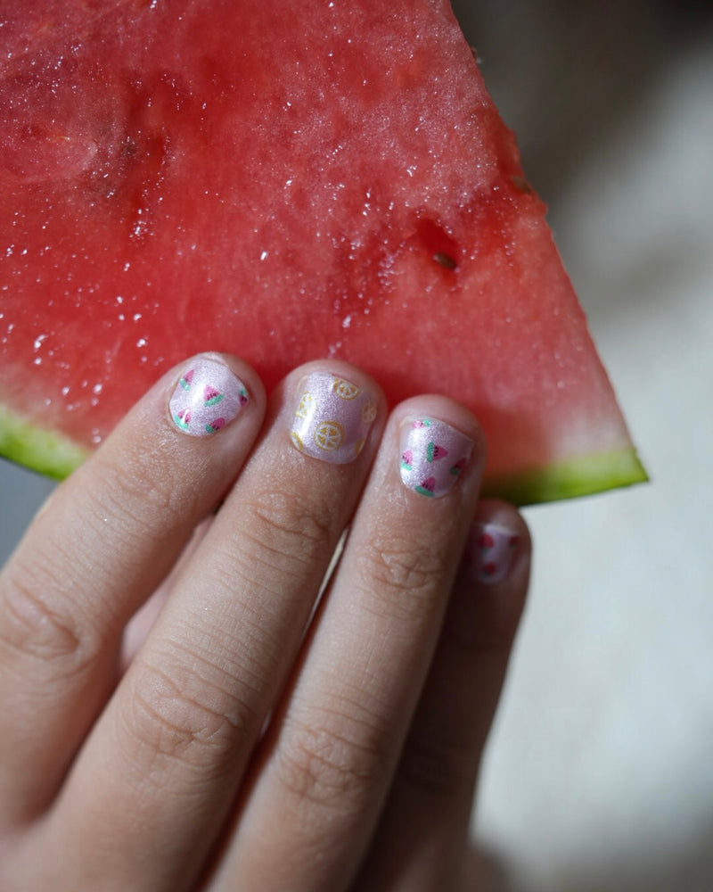 Kinderhand hält ein Stück Wassermelone und zeigt die Sheesh Nails Kinderfolie „Freche Früchtchen“. Die bunten Nagelfolien mit fruchtigen Motiven und Glitzereffekt sorgen für einen verspielten, sommerlichen Look – perfekt für Kinder, die Spaß an kreativer, fröhlicher Maniküre haben.
