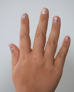 Kinderhand hält ein Set der Sheesh Nails Kinderfolie „Freche Früchtchen“. Die bunten Nagelfolien zeigen fröhliche Fruchtmotive wie Erdbeeren, Zitronen und Kiwis auf transparentem Untergrund. Das verspielte Design steht für Sommer, Spaß und kreative Kinder-Maniküren – ideal für kleine Nagelfans, die farbenfrohe Styles lieben.