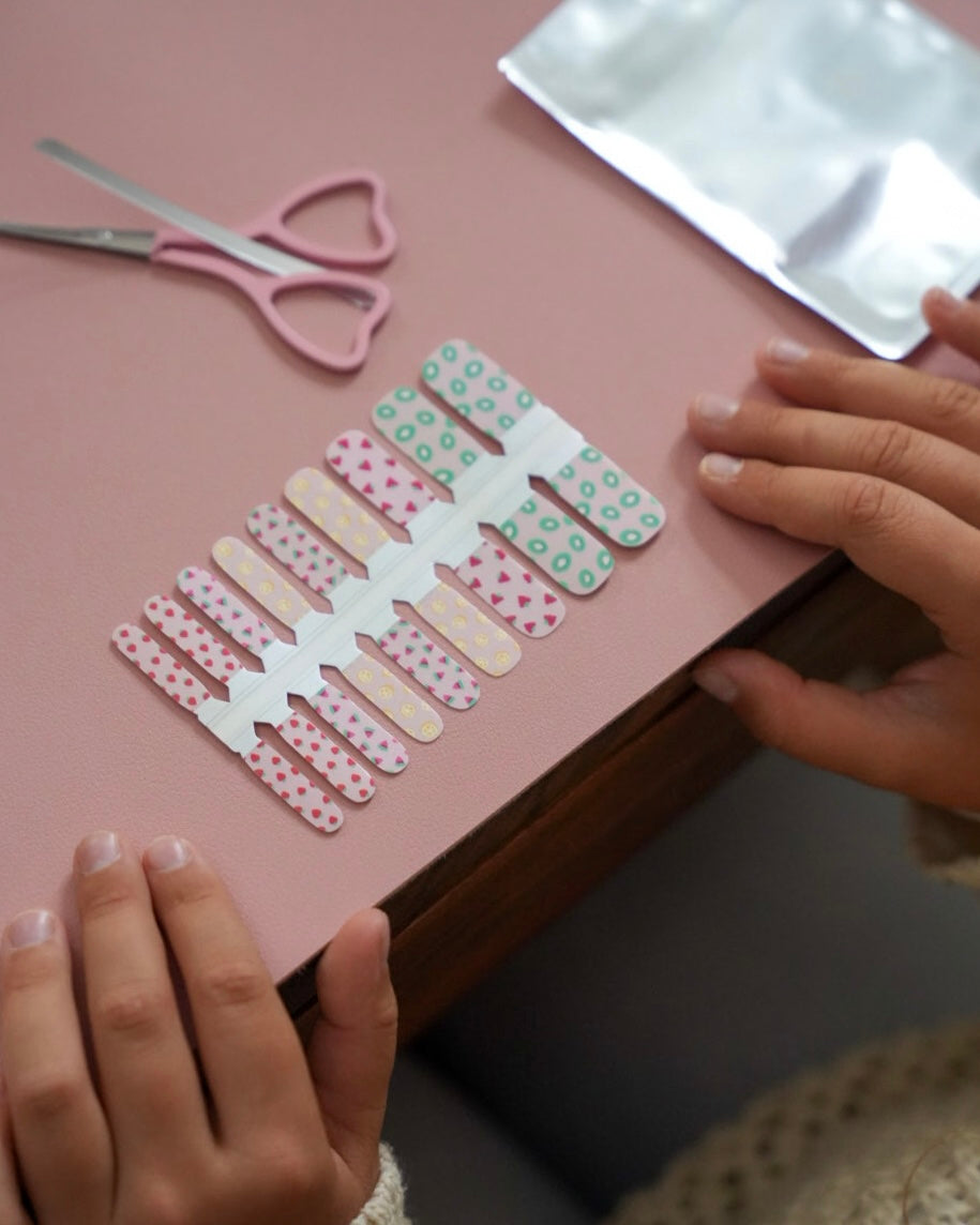 Kinderhände legen bunte Sheesh Nails Kinderfolien „Love“ auf einen rosa Untergrund. Die verspielten Nagelfolien in sanften Rosa-, Grün- und Beigetönen mit Herzmotiven stehen für kreative, liebevoll gestaltete Maniküren – ideal für kleine Nailart-Fans und als kindgerechtes, farbenfrohes Accessoire.