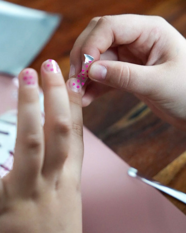 Kinderhand mit Sheesh Nails Kinderfolie „Love“ zeigt zarte, rosafarbene Herzen auf transparentem Untergrund. Die verspielte Maniküre wirkt liebevoll und kreativ – ideal für kleine Nagelfans, die sanfte Farben, süße Motive und kindgerechte Designs lieben.
