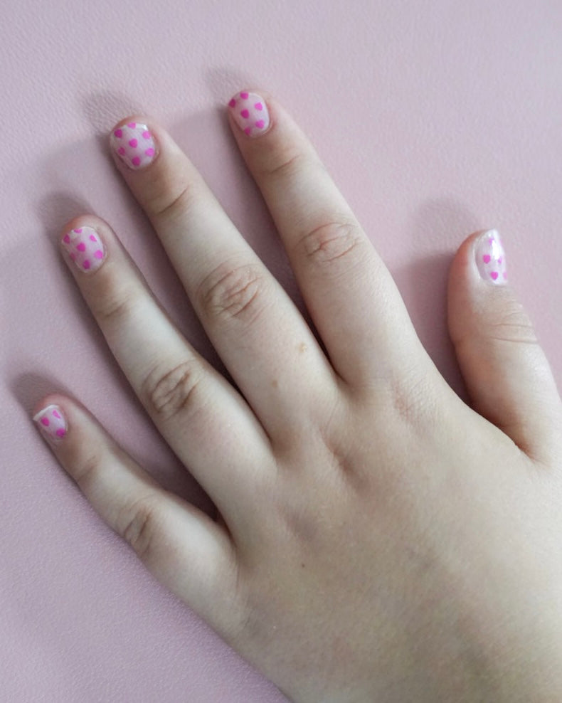 Kinderhand mit rosa Sheesh Nails Kinderfolie „Love“. Die Nagelfolien zeigen kleine, pinke Herzmotive auf transparentem Untergrund und verleihen einen verspielten, liebevollen Look – perfekt für Kinder, die zarte Farben und kreative, herzliche Designs lieben.