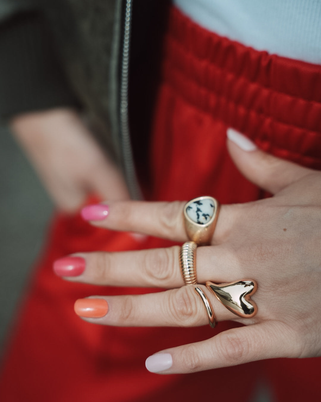 Hand mit mehrfarbiger Maniküre in Pink, Orange und Nude-Tönen, geschmückt mit goldenen Ringen. Die Nägel zeigen die Sheesh Nails Nagelfolien „Farben“ – ein trendiger, sommerlicher Look mit glänzendem Finish, ideal für kreative Nailart und modische Akzente.