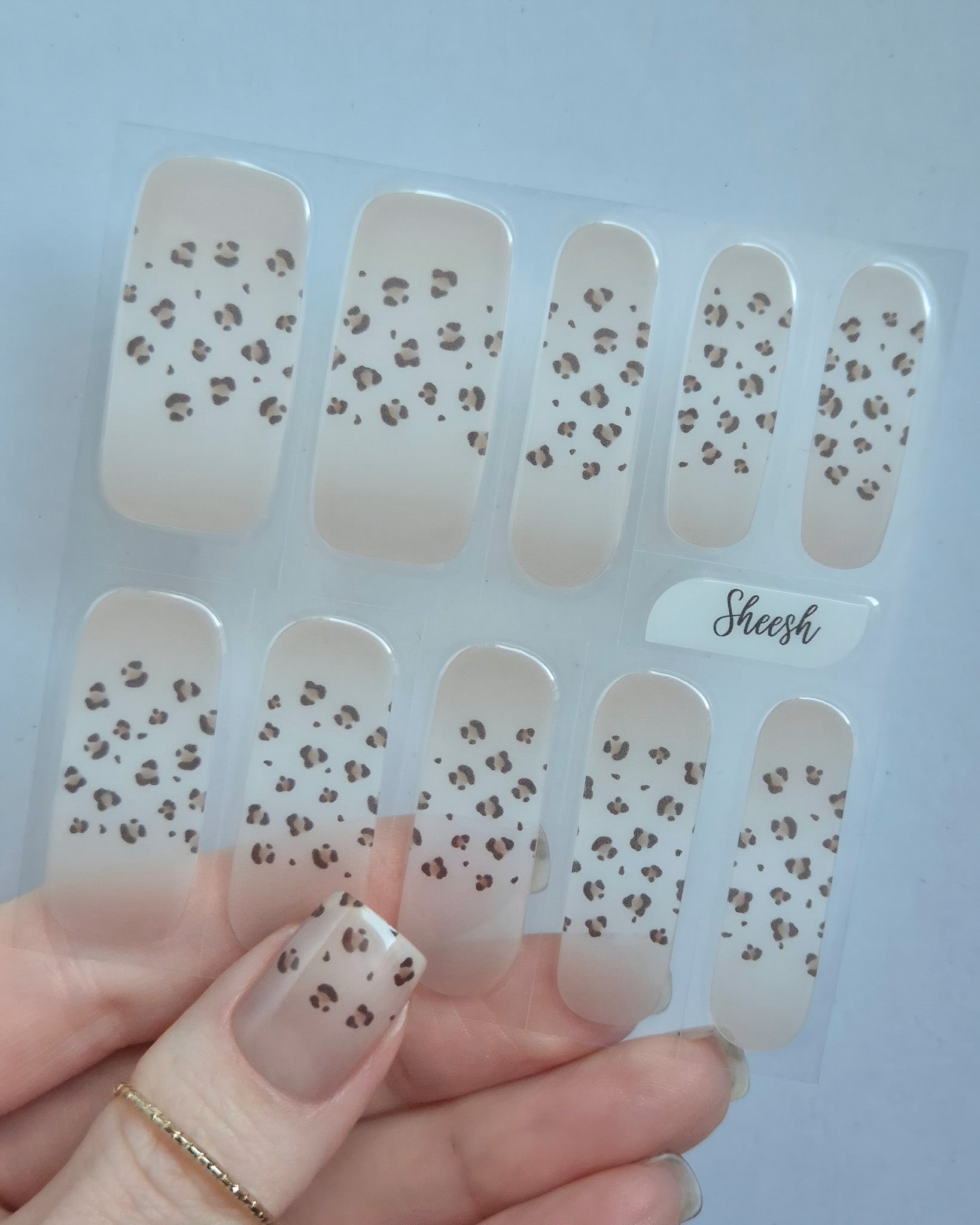 Hand trägt die Sheesh Nails UV-Nagelfolie Half Life. Die Folien zeigen ein transparentes Design mit feinem Leopardenmuster in Braun- und Beigetönen auf zartem Nude-Hintergrund. Der Look wirkt elegant, modern und leicht verspielt – perfekt für trendige Animal-Print-Maniküren mit stilvollem Finish.
