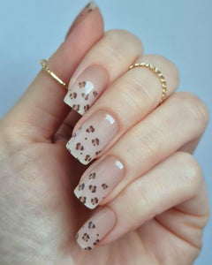 Hand trägt die Sheesh Nails UV-Nagelfolie Half Life. Die Folien zeigen ein transparentes Design mit feinem Leopardenmuster in Braun- und Beigetönen auf zartem Nude-Hintergrund. Der Look wirkt elegant, modern und leicht verspielt – perfekt für trendige Animal-Print-Maniküren mit stilvollem Finish.