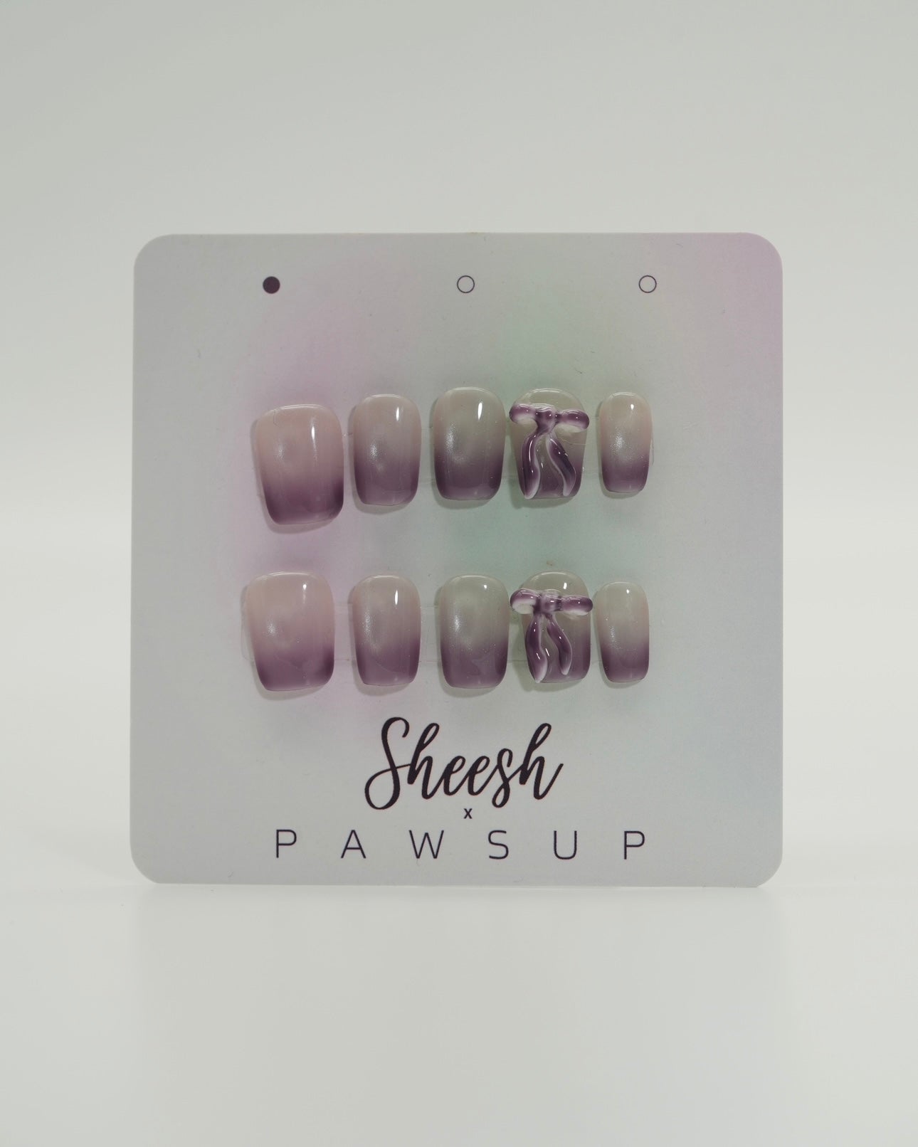 Sheesh Nails x PawsUp Press-on Nails in zartem Flieder- und Nude-Verlauf mit Schleifen-Detail. Hochwertige, wiederverwendbare künstliche Fingernägel im modernen Ombre-Design. Edles Press-on-Set für elegante Maniküre mit femininer Note und sanftem Farbspiel.