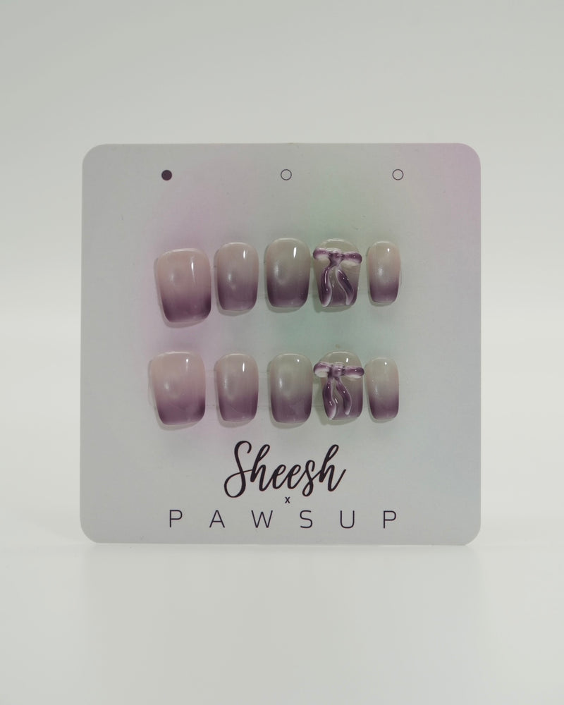 Sheesh Nails x PawsUp Press-on Nails in zartem Flieder- und Nude-Verlauf mit Schleifen-Detail. Hochwertige, wiederverwendbare künstliche Fingernägel im modernen Ombre-Design. Edles Press-on-Set für elegante Maniküre mit femininer Note und sanftem Farbspiel.