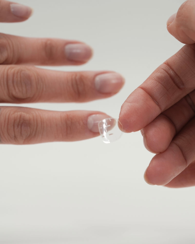 Anbringen von Sheesh Nails Press-on Nails – Nahaufnahme einer Hand, die einen transparenten Klebepad auf den natürlichen Nagel auflegt. Schritt-für-Schritt-Anwendung für wiederverwendbare Press-on Nails, einfache Handhabung und perfekte Vorbereitung für eine haltbare Maniküre zu Hause.
