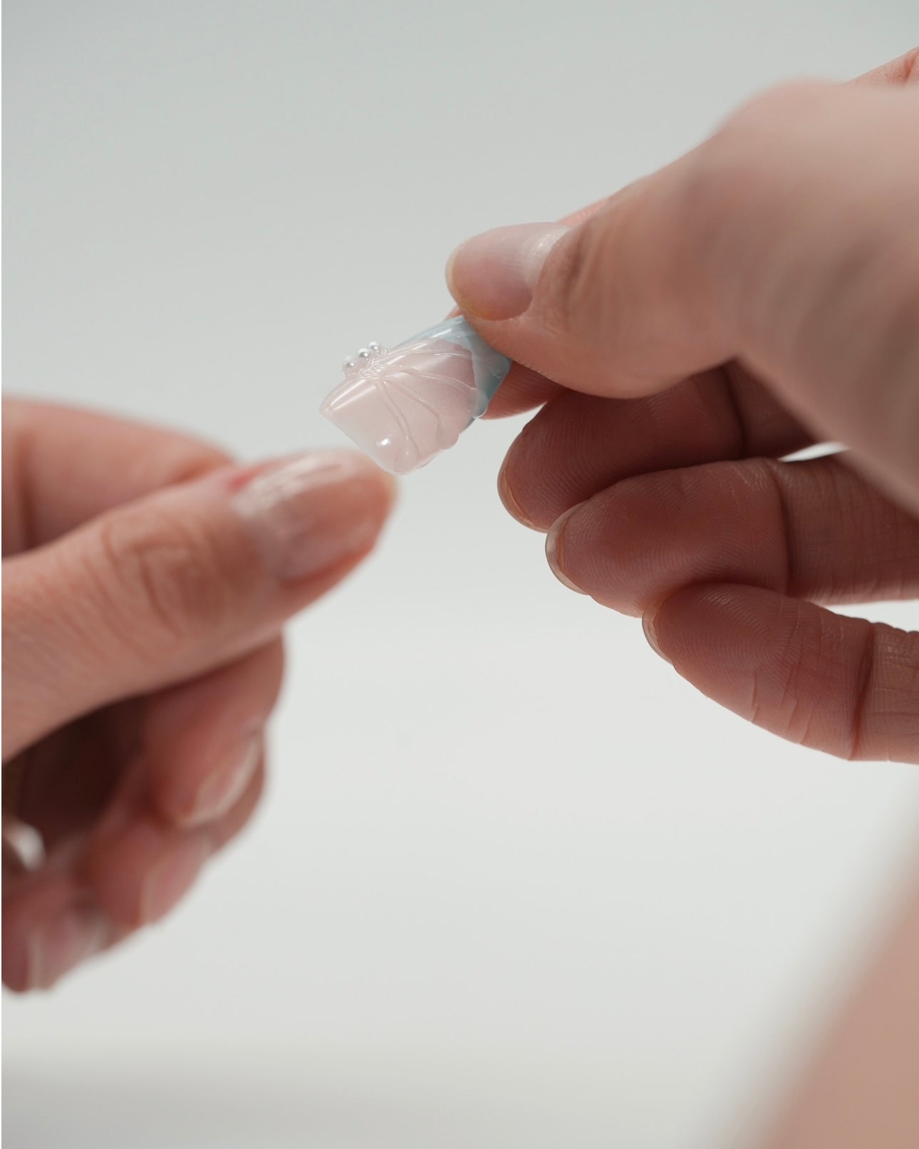 Sheesh Nails Press-on Nails werden auf den natürlichen Nagel aufgesetzt – Schritt-für-Schritt-Anwendung mit Klebepad. Nahaufnahme der Hand beim Anbringen von wiederverwendbaren künstlichen Fingernägeln im modernen Design. Anleitung für einfache, schnelle Maniküre zu Hause mit Sheesh Nails Press-ons.