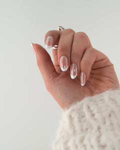 Sheesh Nails Press-on Nails in klassischem French-Design mit transparentem Glanzfinish. Hand mit cremefarbenem Strickpullover zeigt elegante, wiederverwendbare künstliche Fingernägel mit weißer French-Spitze. Zeitloses Nageldesign für gepflegte Hände – natürliche Eleganz und professionelle Maniküre für jeden Anlass.