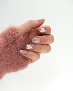 Sheesh Nails Press-on Nails in Rosé mit weißen Blüten und schimmerndem Glanzfinish. Hand in rosa Strickpullover zeigt elegante, wiederverwendbare künstliche Fingernägel im femininen Blumendesign. Hochwertige Press-ons für eine natürliche, gepflegte Maniküre mit edlem, romantischem Look.
