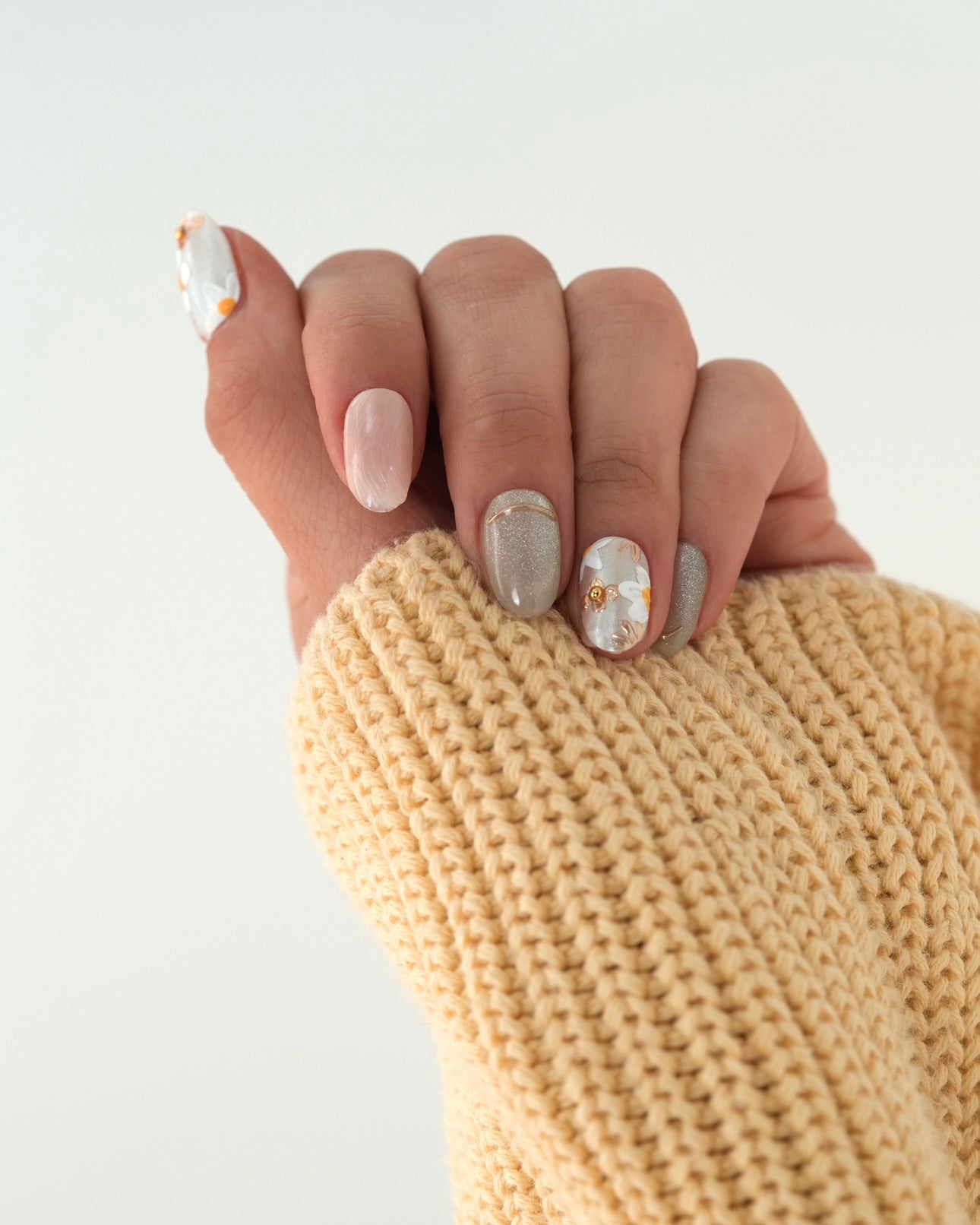 Sheesh Nails Press-on Nails in Beige, Grau und Weiß mit goldenen Details und Marmor-Effekt. Hand mit kuscheligem gelbem Strickpullover zeigt gepflegte, elegante Press-ons mit Glanzfinish. Wiederverwendbare künstliche Fingernägel im modernen Design – perfekte Kombination aus Natürlichkeit und Luxus.