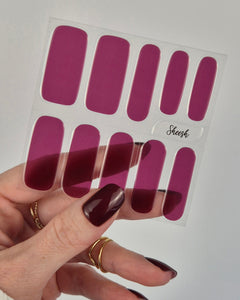 Hand mit dunkel lackierten Nägeln hält ein Set violett-pinker Nagelfolien „L.A. by night“ von Sheesh Nails vor hellem Hintergrund. Die UV-Nagelfolien zeichnen sich durch ihre intensive Farbe und glänzende Oberfläche aus – perfekt für einen ausdrucksstarken, modernen Look.