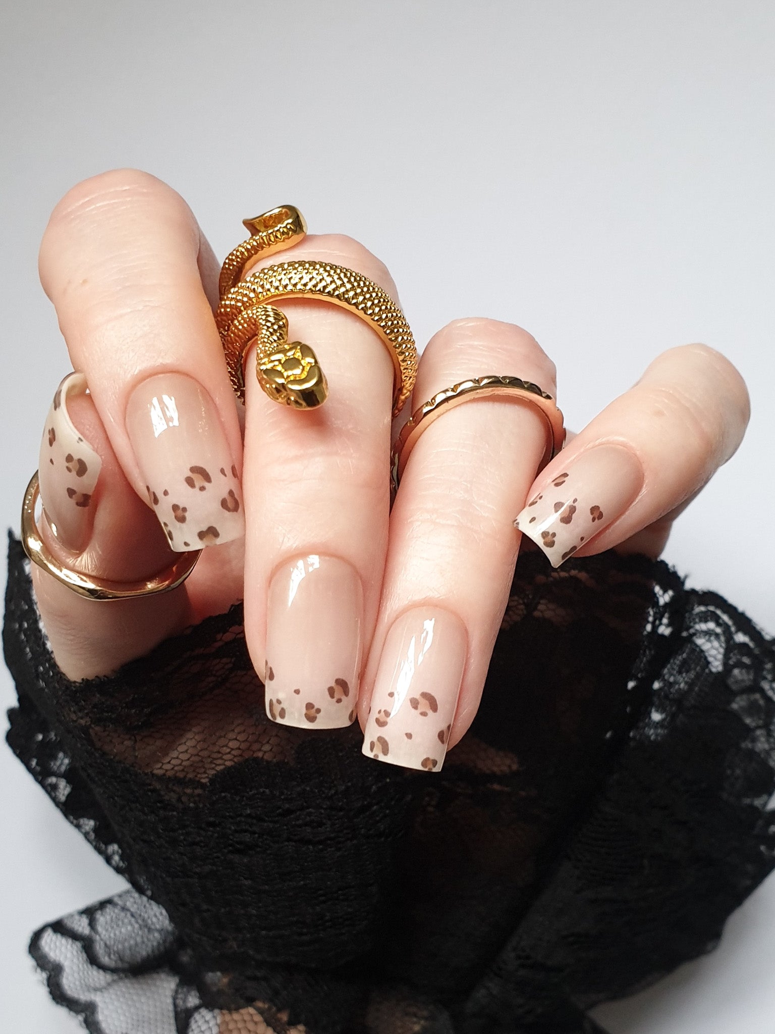 Hand trägt die Sheesh Nails UV-Nagelfolie Half Life. Die Folien zeigen ein transparentes Design mit feinem Leopardenmuster in Braun- und Beigetönen auf zartem Nude-Hintergrund. Der Look wirkt elegant, modern und leicht verspielt – perfekt für trendige Animal-Print-Maniküren mit stilvollem Finish.