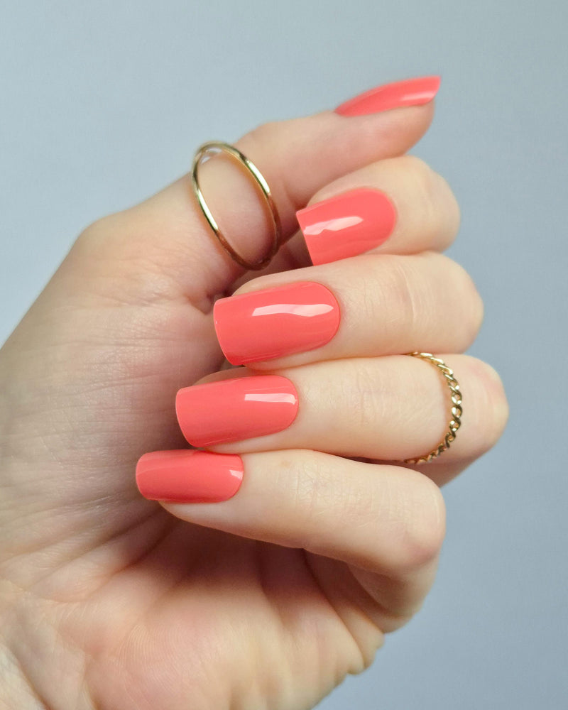 UV Nagelfolien in leuchtendem Korallrot – SHEESH Nails „Lobster Roll“. Hand hält glänzende korallrote Gel-Nagelfolien auf transparenter Trägerfolie. Intensive Sommerfarbe, vegan, selbstklebend und lang haltbar für perfekte Maniküre zuhause.