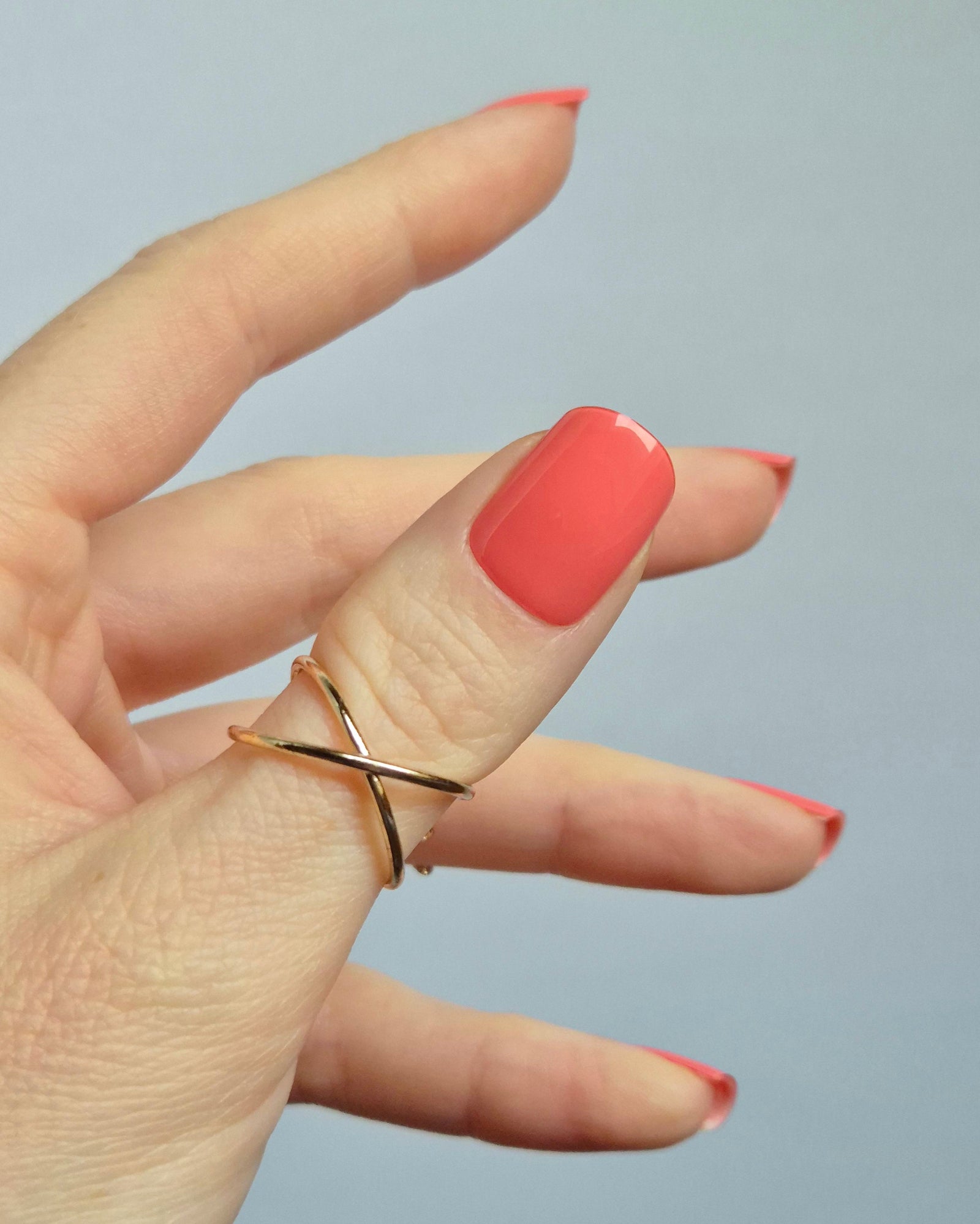 Hand mit korallroter UV-Maniküre von SHEESH Nails – „Lobster Roll“. Glänzende, gleichmäßig aufgetragene Gel-Nagelfolien in intensivem Korallton. Vegane, selbstklebende und lang haltbare Maniküre für ein sommerlich frisches Nail-Design zuhause.