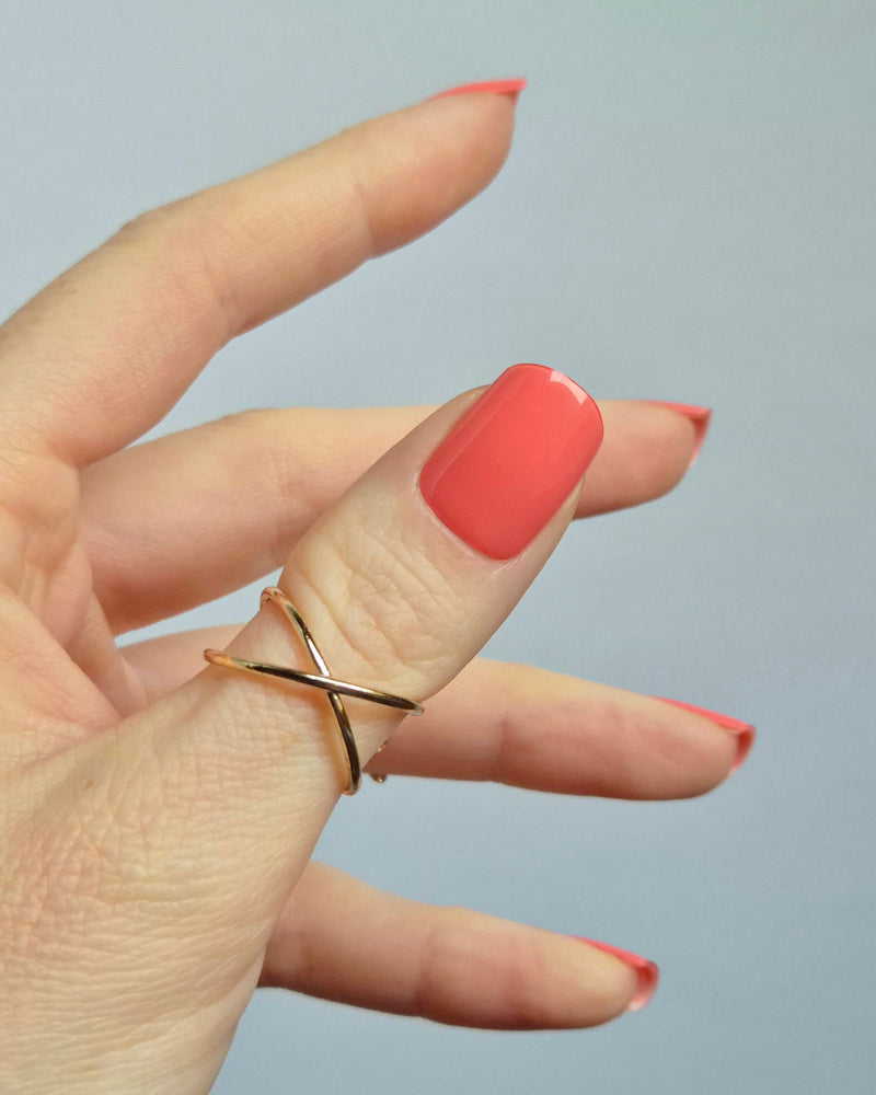 Hand mit korallroter UV-Maniküre von SHEESH Nails – „Lobster Roll“. Glänzende, gleichmäßig aufgetragene Gel-Nagelfolien in intensivem Korallton. Vegane, selbstklebende und lang haltbare Maniküre für ein sommerlich frisches Nail-Design zuhause.