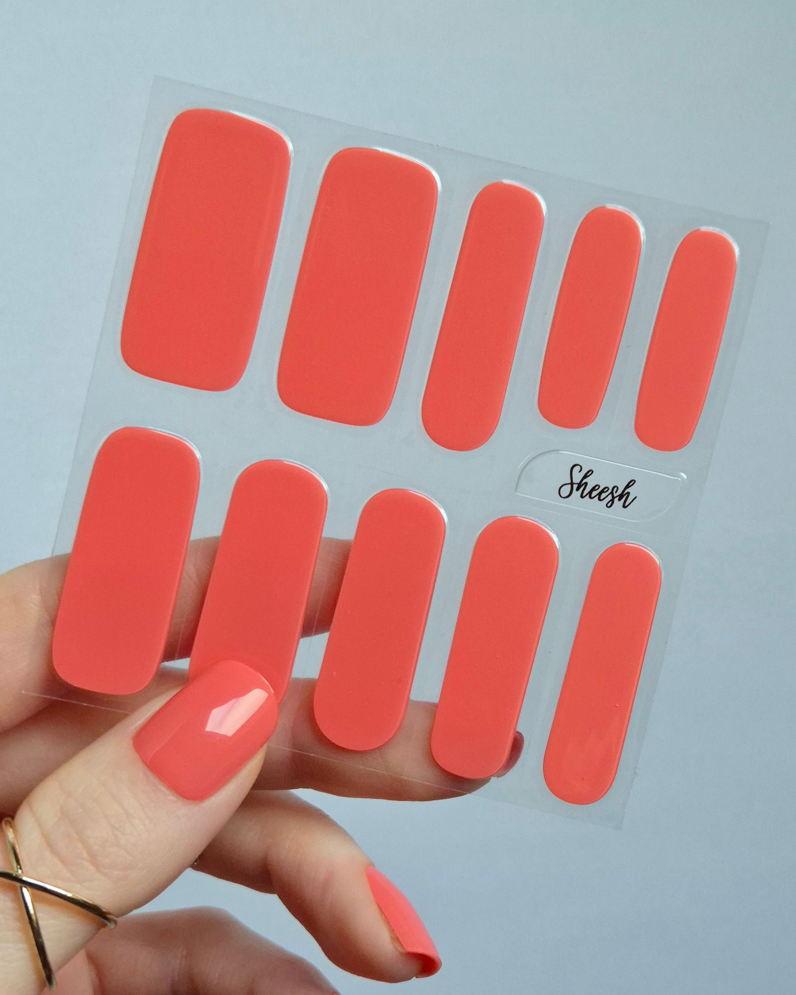 UV Nagelfolien in leuchtendem Korallrot – SHEESH Nails „Lobster Roll“. Hand hält glänzende korallrote Gel-Nagelfolien auf transparenter Trägerfolie. Intensive Sommerfarbe, vegan, selbstklebend und lang haltbar für perfekte Maniküre zuhause.
