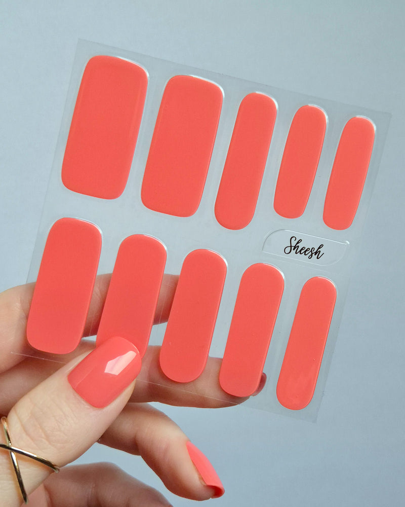 UV Nagelfolien in leuchtendem Korallrot – SHEESH Nails „Lobster Roll“. Hand hält glänzende korallrote Gel-Nagelfolien auf transparenter Trägerfolie. Intensive Sommerfarbe, vegan, selbstklebend und lang haltbar für perfekte Maniküre zuhause.