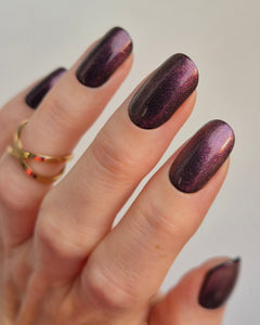 Hand mit dunkelviolett schimmernden Nägeln trägt die Sheesh Nails UV-Nagelfolie „Midnight“, veredelt mit dem Topcoat „Glitter & Grit“. Der Look kombiniert tiefen Metallic-Glanz mit feinem Glitzereffekt und spiegelt ein elegantes, luxuriöses Finish wider – ideal für Abendstyles und glamouröse Auftritte.