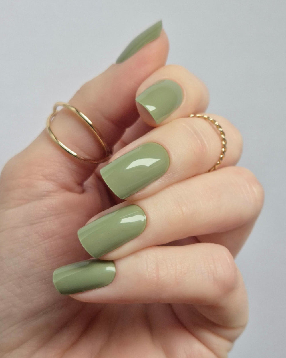 Hand mit olivgrüner UV-Maniküre von SHEESH Nails – glänzende, gleichmäßige Nägel mit „Olives from Napa“ Nagelfolien. Moderne, elegante Maniküre mit Goldringen, vegan, haltbar und ohne Aushärten.