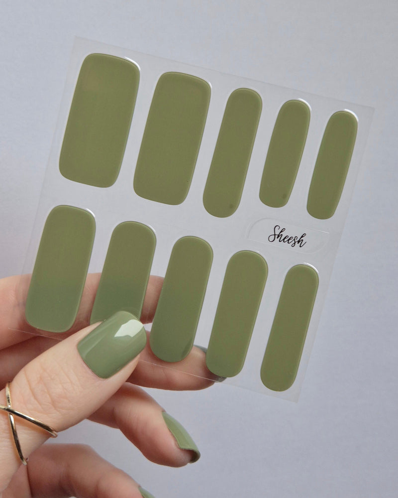 UV Nagelfolien in Olivgrün – SHEESH Nails „Olives from Napa“. Hand hält glänzende olivgrüne Gel-Nagelfolien auf transparenter Trägerfolie. Perfekte Maniküre ohne Lack, vegan, lang haltbar und einfach anzuwenden.