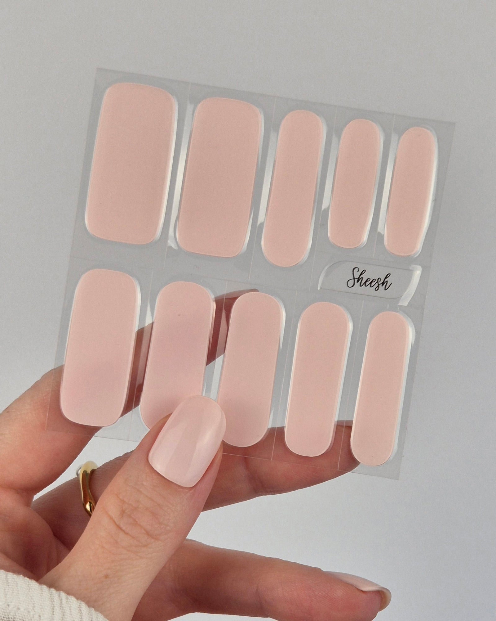 Hand mit hellrosa lackierten Nägeln hält ein Set der Sheesh Nails UV-Nagelfolie „Pale Turn“. Die sanften, pastelligen Folien mit zartem Glanz verleihen einen gepflegten, natürlichen Look – ideal für dezente Maniküren, Alltagsstyles und elegante Anlässe.