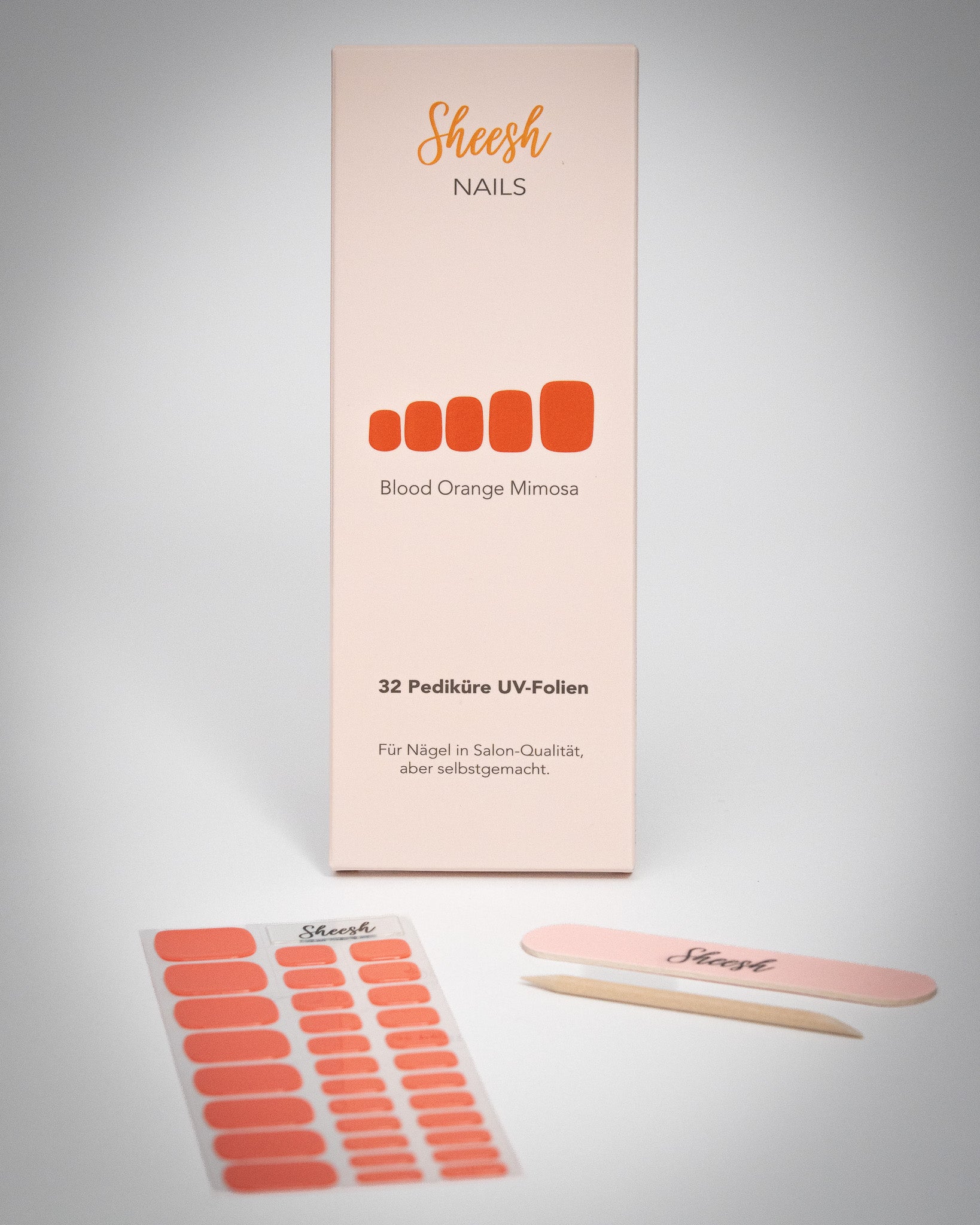 Produktaufnahme der Sheesh Nails Pedi UV-Nagelfolie „Blood Orange Mimosa“. Die Verpackung zeigt das elegante Design in Korallrot-Orange, kombiniert mit Feile und Folienbogen. Das Bild vermittelt Qualität, Frische und sommerliche Energie – ideal für eine moderne, gepflegte Pediküre im leuchtenden Statement-Look.