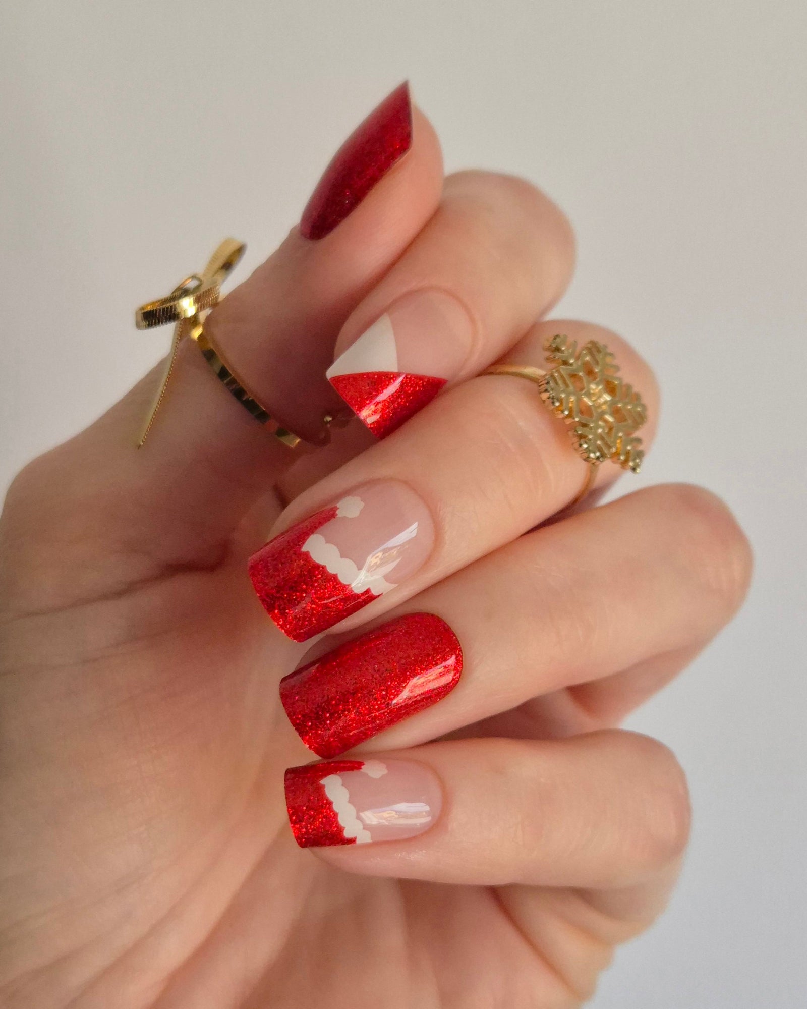 Nahaufnahme einer Hand mit roten, glitzernden Nagelfolien im Santa-Stil. Einige Nägel zeigen weiße Zierlinien und Details, die an das Fell des Weihnachtsmanns erinnern. Der Look kombiniert festlichen Glamour mit verspielter Leichtigkeit.