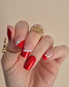 Nahaufnahme einer Hand mit roten, glitzernden Nagelfolien im Santa-Stil. Einige Nägel zeigen weiße Zierlinien und Details, die an das Fell des Weihnachtsmanns erinnern. Der Look kombiniert festlichen Glamour mit verspielter Leichtigkeit.