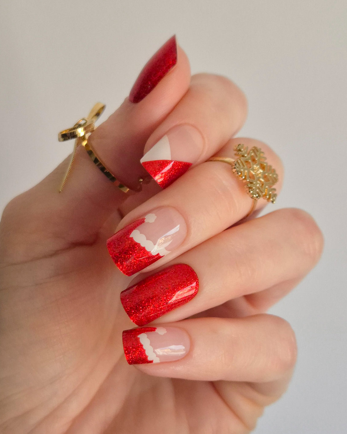 Nahaufnahme einer Hand mit roten, glitzernden Nagelfolien im Santa-Stil. Einige Nägel zeigen weiße Zierlinien und Details, die an das Fell des Weihnachtsmanns erinnern. Der Look kombiniert festlichen Glamour mit verspielter Leichtigkeit.