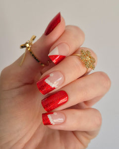 Nahaufnahme einer Hand mit roten, glitzernden Nagelfolien im Santa-Stil. Einige Nägel zeigen weiße Zierlinien und Details, die an das Fell des Weihnachtsmanns erinnern. Der Look kombiniert festlichen Glamour mit verspielter Leichtigkeit.
