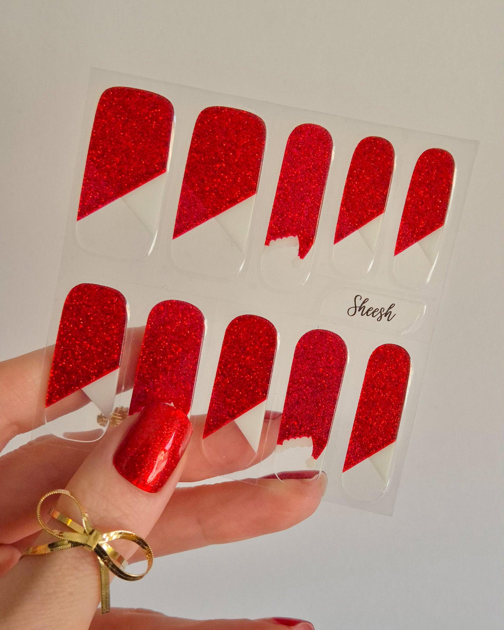 Nahaufnahme einer Hand mit roten, glitzernden Nagelfolien im Santa-Stil. Einige Nägel zeigen weiße Zierlinien und Details, die an das Fell des Weihnachtsmanns erinnern. Der Look kombiniert festlichen Glamour mit verspielter Leichtigkeit.