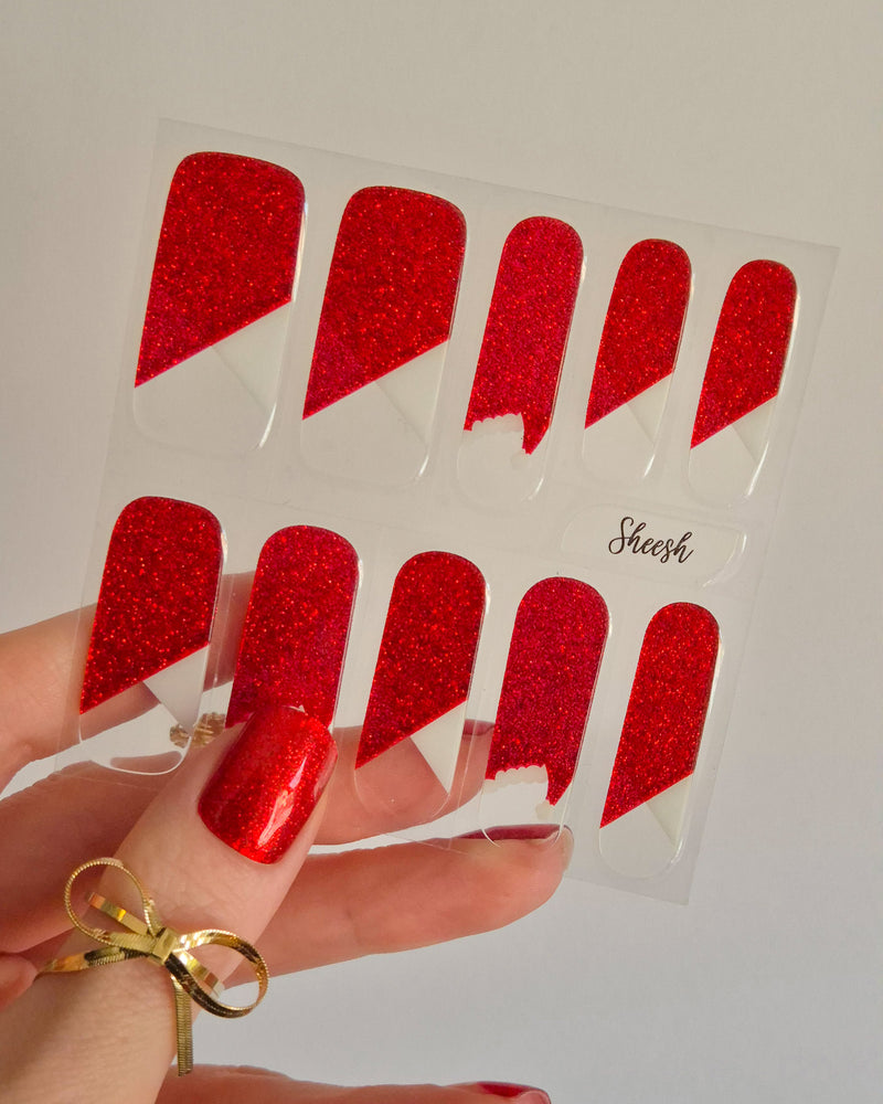 Nahaufnahme einer Hand mit roten, glitzernden Nagelfolien im Santa-Stil. Einige Nägel zeigen weiße Zierlinien und Details, die an das Fell des Weihnachtsmanns erinnern. Der Look kombiniert festlichen Glamour mit verspielter Leichtigkeit.