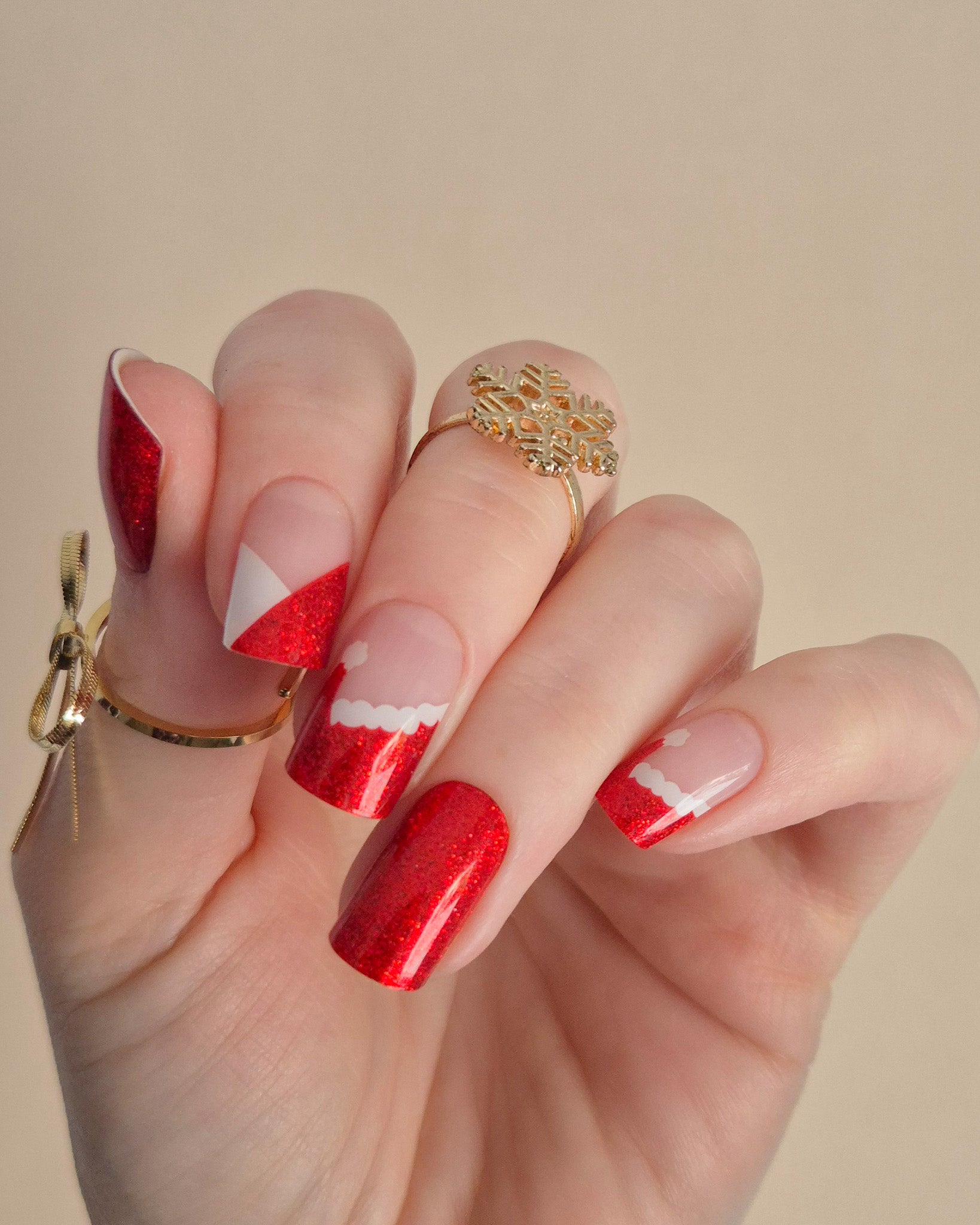Nahaufnahme einer Hand mit roten, glitzernden Nagelfolien im Santa-Stil. Einige Nägel zeigen weiße Zierlinien und Details, die an das Fell des Weihnachtsmanns erinnern. Der Look kombiniert festlichen Glamour mit verspielter Leichtigkeit.