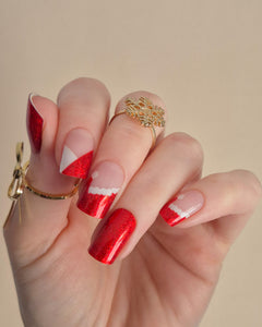 Nahaufnahme einer Hand mit roten, glitzernden Nagelfolien im Santa-Stil. Einige Nägel zeigen weiße Zierlinien und Details, die an das Fell des Weihnachtsmanns erinnern. Der Look kombiniert festlichen Glamour mit verspielter Leichtigkeit.